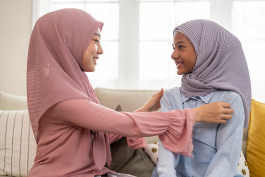 Muslim mother adjusting hijab for daughter on sofa, islamic parenting and love in family moment, smiling faces show joy and nurturing connection in home, teaching islamic values with love and care