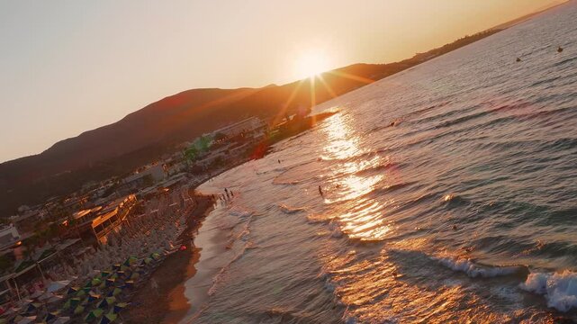 Golden sunset over Stalida, Crete, with waves lapping the shore, beach umbrellas, and small buildings reflecting the warm sunlight.