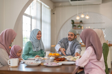 Muslim big family sharing traditional meal together around dining table wearing hijabs and kufi in...