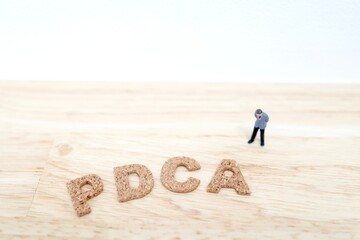 PDCAを考えるビジネスマンのミニチュアと木製文字