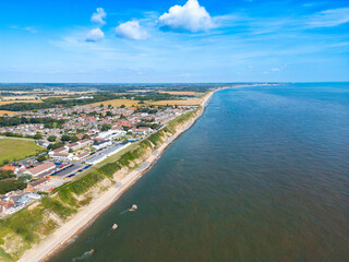 UAV view of a sunny Norfolk, UK coastline in early August. Holiday chalets and a resort can be seen near the cliff edge.