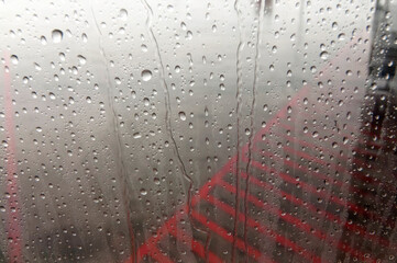 Raindrops clinging to glass on a gloomy day with red structure behind