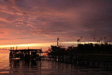 Obraz premium Stunning sunset at the harbor with cargo ship on calm water surface