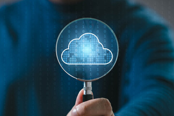 A person holds a magnifying glass over a digital cloud, symbolizing cloud computing and data...
