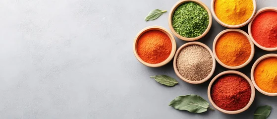 Assorted ground spices in wooden bowls. Different vibrant colors. Green leaves. Gray surface. Cooking ingredients. Top view. Preparation of food. Seasoning collection. © Tetiana