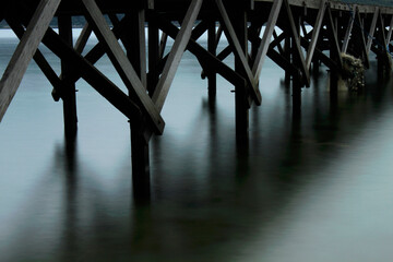 Tranquil waters flow under rustic wooden pier creating peaceful scene