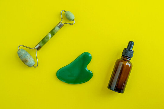 Bottle for cosmetics and jade massagers on a yellow background. Beauty saloon. Background with copy space.