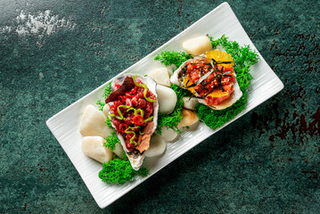 Gourmet seafood appetizers served in oyster shells on a white plate, garnished with chili, seaweed, and citrus. Elegant food presentation on dark green background