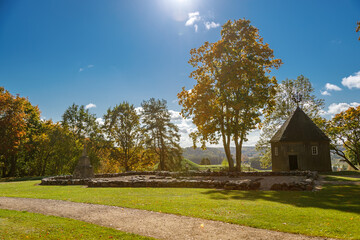 Sunlit autumn landscape in Kernave, Lithuania, featuring a historic wooden chapel, ancient mound remnants