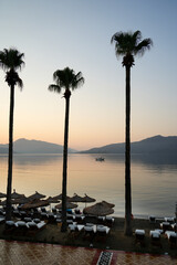 Tall palm trees are silhouetted against a golden sunrise sky at a tranquil beach resort. This...