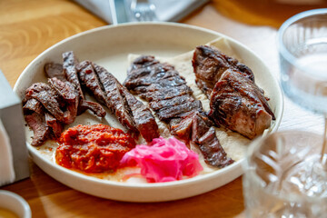 Beef pieces of meat, tomato sauce and red cabbage salad all on a white plate 