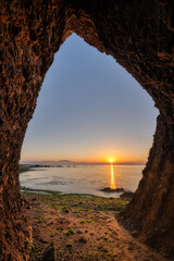 Rocky Coastal Arch Framing Peaceful Ocean Sunrise with Green Seaweed