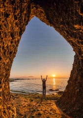 Silhouetted Person Celebrating Sunrise Through Natural Cave Opening Overlooking Ocean