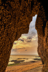 Rocky Coastal Arch Framing Peaceful Ocean Sunrise with Green Seaweed