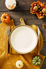 Autumn table setting with empty plate with cutlery, pumpkins, dried flowers, candle, acorns,...