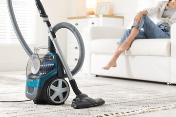 Woman resting on sofa at home, focus on vacuum cleaner