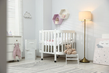 Stylish white crib, chest of drawers, lamp, toys and decor elements in baby's room. Interior design