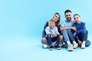 Fototapeta premium Happy parents and their children sitting on light blue background, space for text. Family