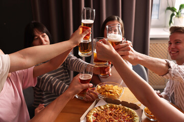 Group of happy friends clinking glasses of beer at table indoors, selective focus