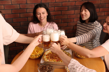 Group of happy friends clinking glasses of beer at table with food indoors, selective focus