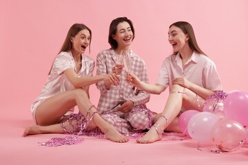 Pajama party. Happy friends with balloons and tinsel clinking glasses on pink background