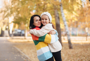 Naklejka premium Cute little girl and mom hugging in the autumn park. Family have fun outdoor.