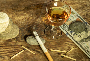 On an old board there is a lit cigarette on a stone, a hundred dollar bill, a glass of cognac and...