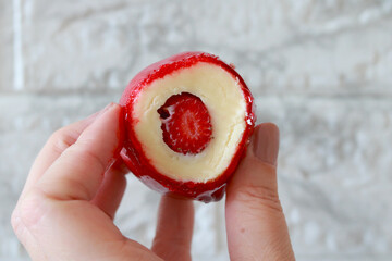 Hand holding a candied strawberry filled with creamy white chocolate, a tempting Brazilian sweet...
