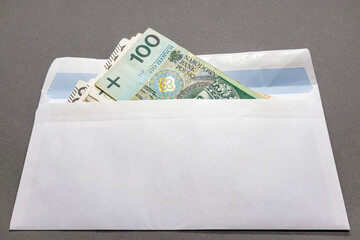Banknotes of Polish currency in denominations of one hundred and two hundred zlotys in a white envelope on a gray background. Polish zloty close-up.