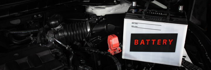Car battery installation in engine bay, white automotive battery with red positive terminal cover,...