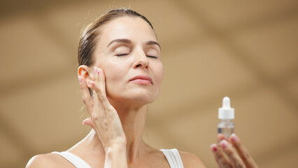 Woman applying skincare serum to her face, enjoying a moment of self-care in a serene wellness...