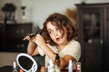 Cute little girl cutting her hair with scissors at home