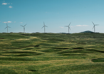 Wind turbines on a green hillside under a clear blue sky. Concept of renewable energy, sustainability and clean power generation. 