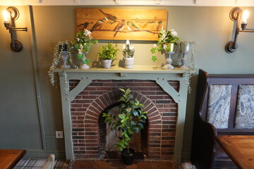 Thurgarton, Nottinghamshire, England – August 18 2025: Cozy rustic fireplace with potted plants...