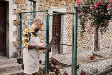 Modern farmer working on laptop while caring for chickens in a rural countryside setting