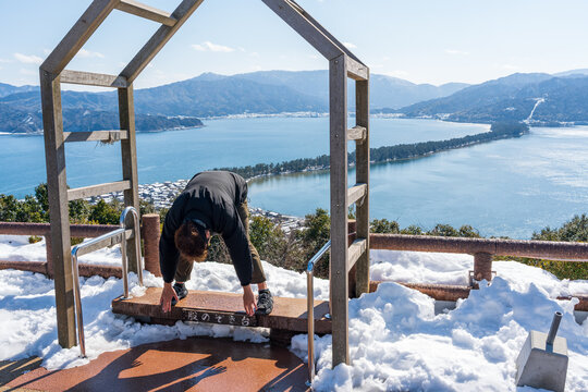 A man performs the traditional "matanozoki" ritual, bending over to view the Amanohashidate sandbar upside-down from Kasamatsu Park. Miyazu, Kyoto, Japan. Japanese translation : matanozoki platform.