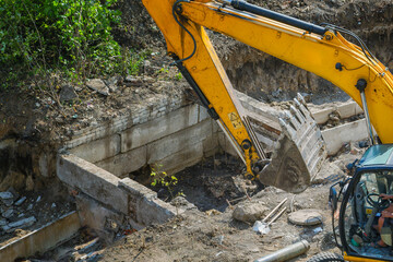Excavator cabin and bucket over dug foundation at construction site, underground utility repair...