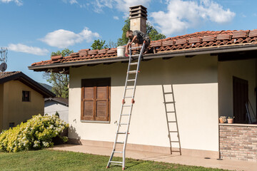 Roofer inspecting and repairing roof on a sunny day, house maintenance work.