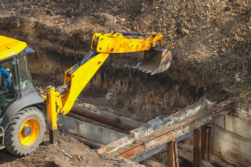  Excavator bucket above dug pit at construction site during repair works of public utilities and...