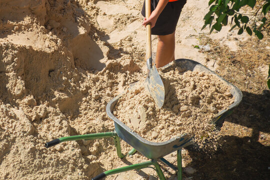 Worker fills wheelbarrow with sand using shovel close-up, sand at construction site, sand as construction material, sand delivery and loading.