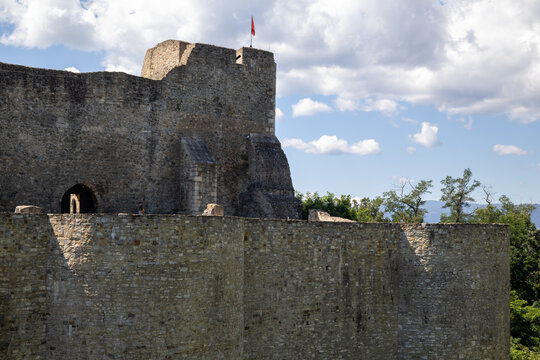 section of Neamț Fortress in Romania. Weathered stone walls and a tower with a lone flag reach towards a partly cloudy sky. - Powered by Adobe