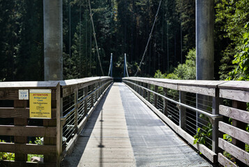 Suspension bridge in forest. Shared hiking trail for hikers, mountain biking and horses with bridge load limit sign. Seymore river suspension bridge, North Vancouver, BC, Canada. Selective focus.