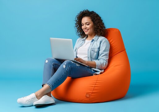 Young woman with curly hair sitting on an orange beanbag chair with a laptop