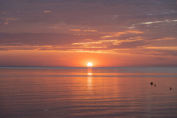 Luc-Sur-Mer, France - 08 07 2025: Panoramic view of the sunrise over the sea with reflections of colorful light, the sun and Le Havre far away