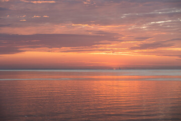 Naklejka premium Luc-Sur-Mer, France - 08 07 2025: Panoramic view of the sunrise over the sea with reflections of colorful light, the sun and Le Havre far away