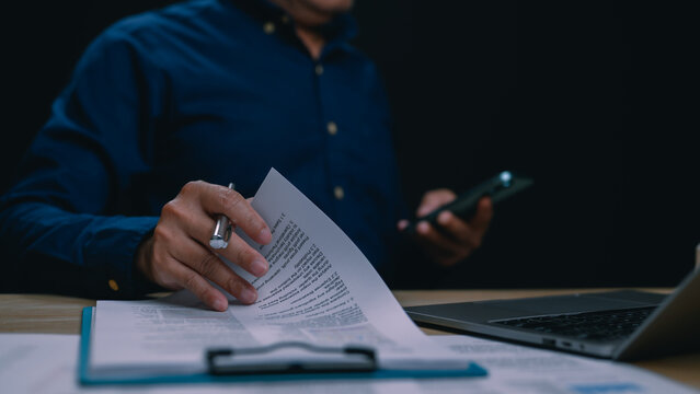 Businessman reviewing legal contract before signing agreement. Professional male manager holding pen, analyzing financial report at office desk. Corporate executive working late, checking documents,