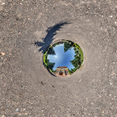 creative tiny planet photo of a rural landscape with dirt road, green fields, and cloudy sky forming a circular world.