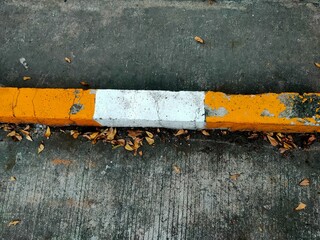 Close-up of a weathered concrete curb painted yellow with a central white block, cracked peeling...