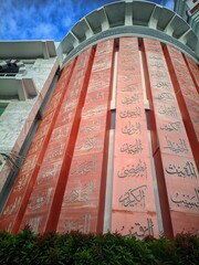 Modern mosque with curved facade and vibrant calligraphy panels. A tall minaret rises beside a...