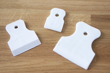 three different-sized white plastic scrapers isolated on wooden background